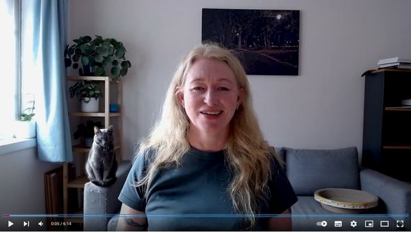 A screenshot of a video of Donna with a grey cat in the background.